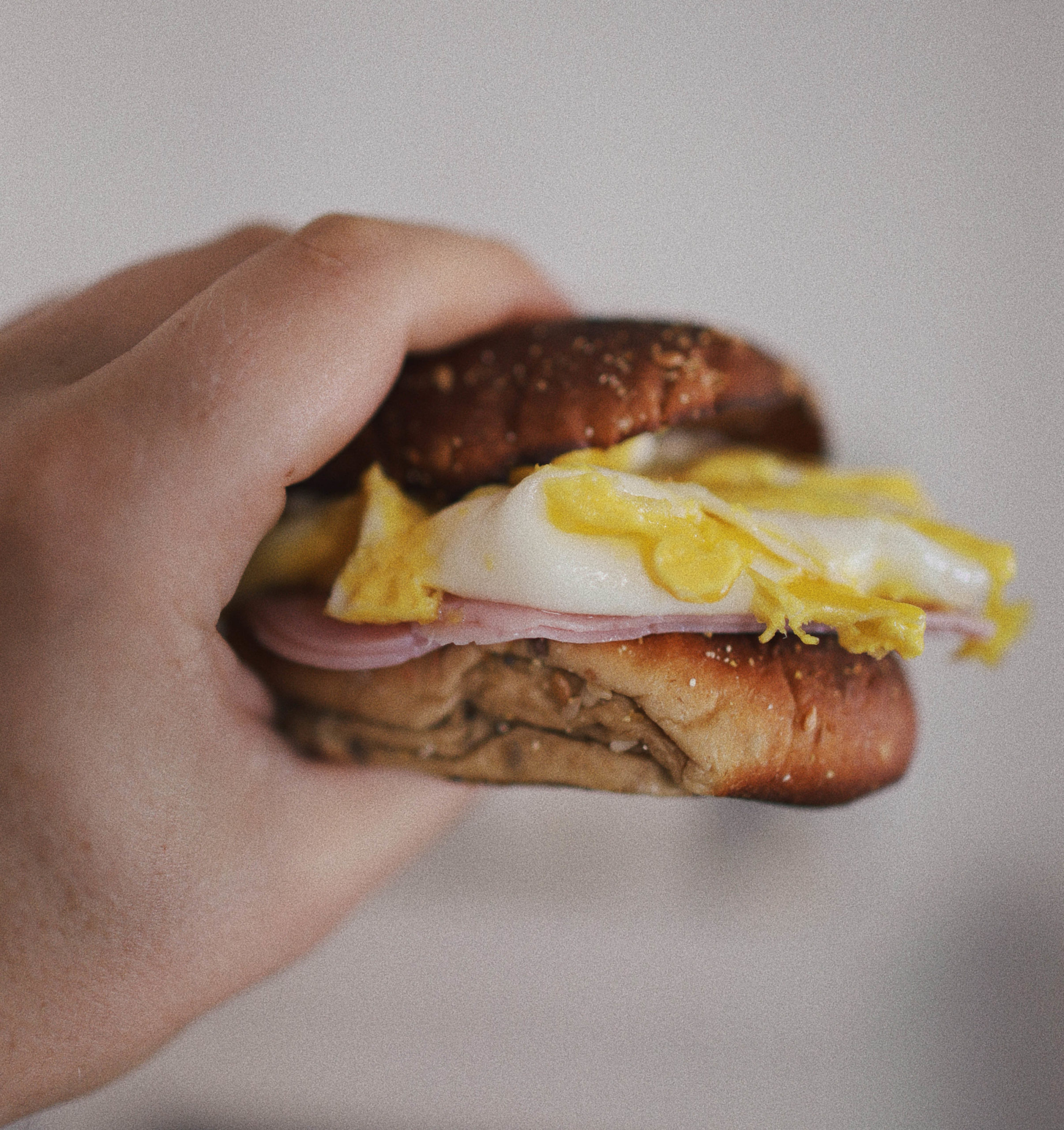 A person holding a Bagel Sandwich with eggs and bacon